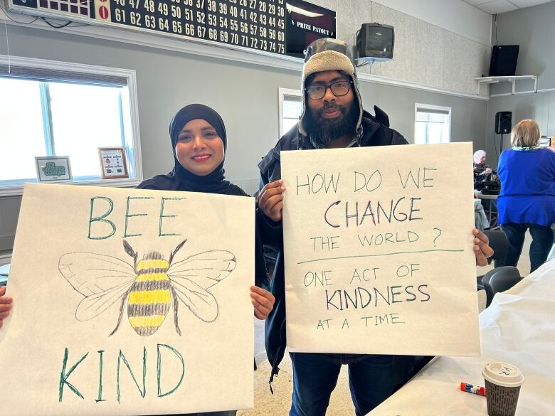 A man and a woman smile and hold signs about kindness