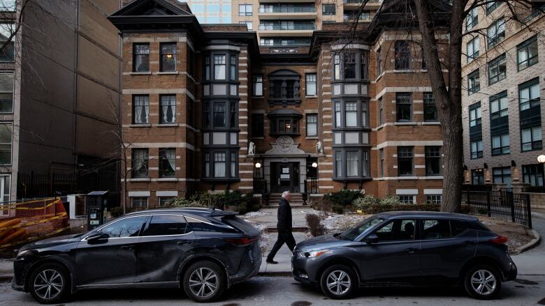 A pedestrian walks down  a city sidewalk in front of an apartment building.