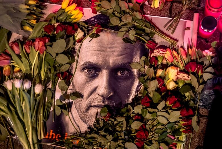 A photo of a man's face is ringed by real-life roses and other flowers.