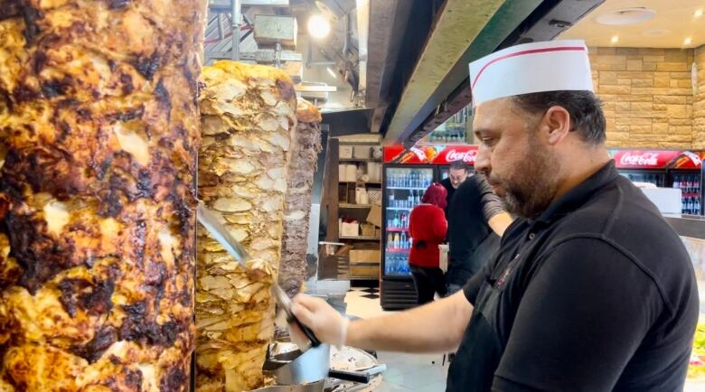 A restaurant worker slices pieces of meat off a spit.