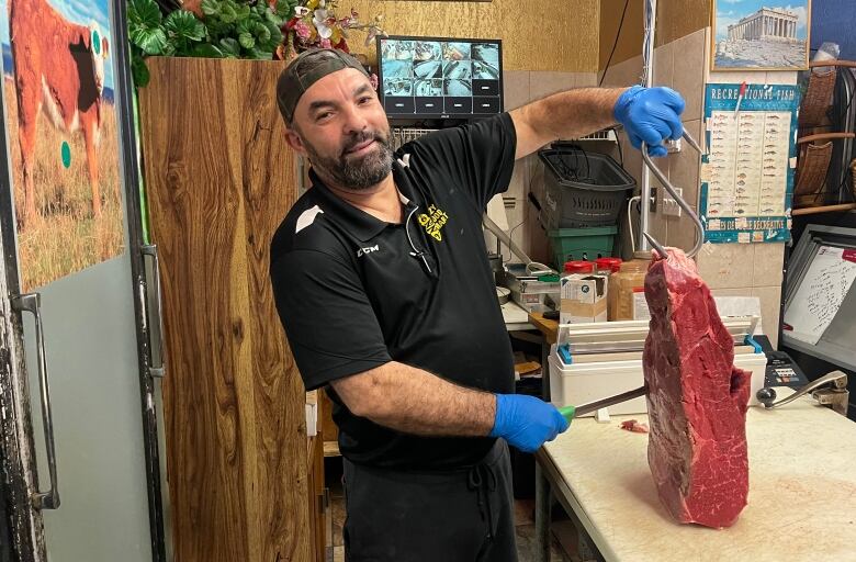 A shawarma shop owners holds up a slab of raw meat.