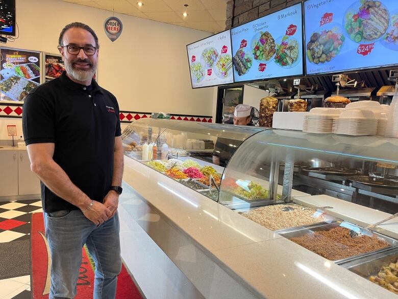 A shawarma shop owner poses next to a counter. 