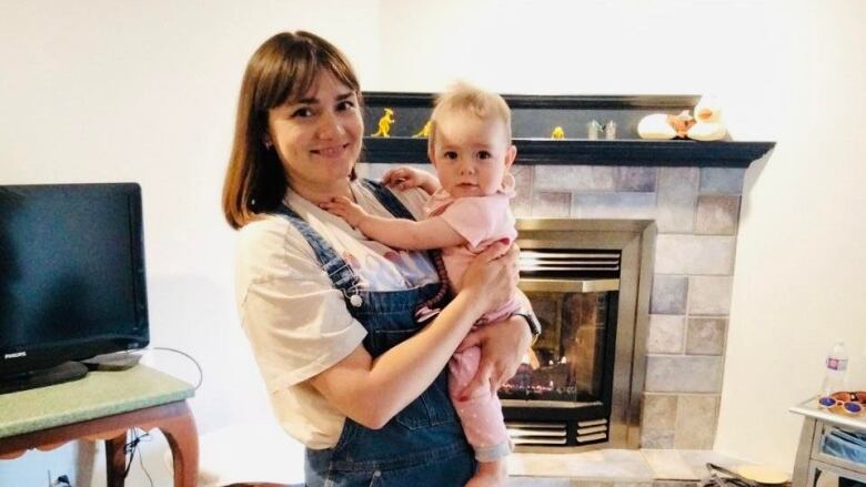 A woman stands in a living room holding a baby.