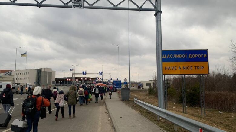 A long line of people walk on a road holding their belongings. 