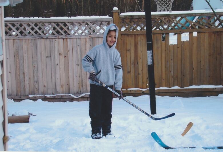 A South Asian child holds a hockey stick in a backyard amid heavy snow.