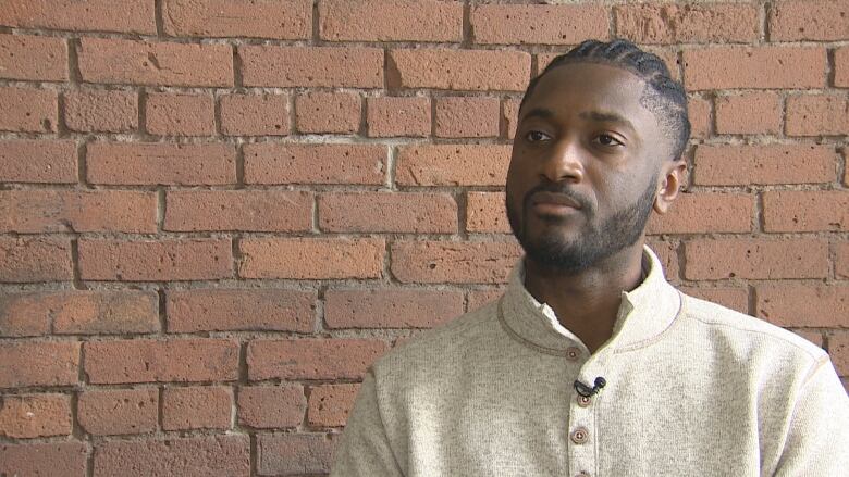 An African Nova Scotian man is seating in front of a brick wall.