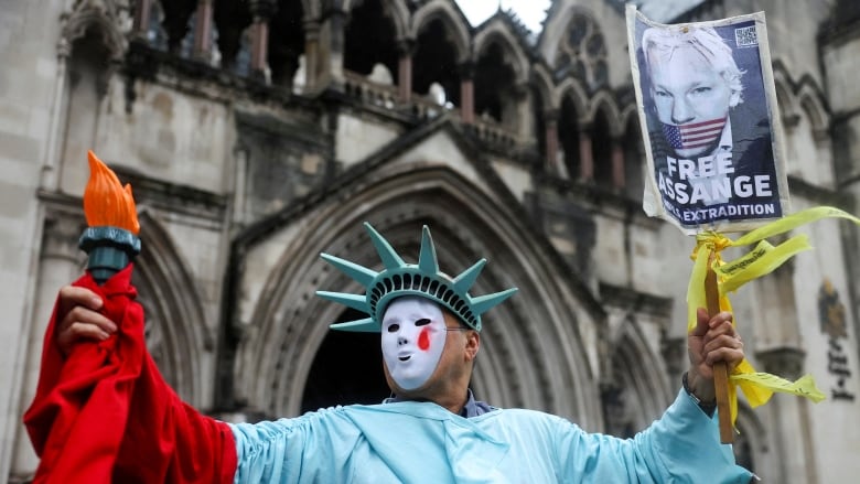 A protester in costume as the Statue of Liberty holds a fake torch in one hand and a free Julian Assange sign in another.