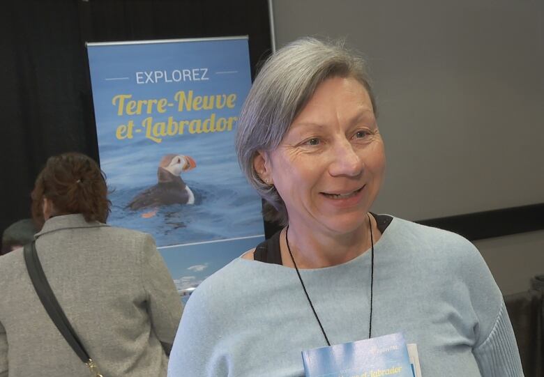 Woman in blue smiling behind a blue poster.