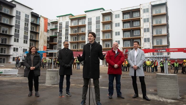 Five people standing in front of a new-build condo, half under construction. 