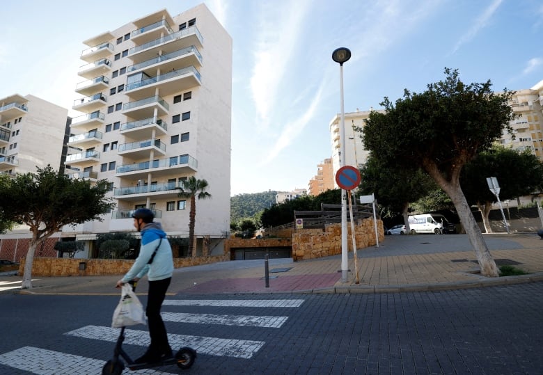 A person rides a scooter past a building in southeastern Spain where Russian pilot Maxim Kuzminov was found dead.