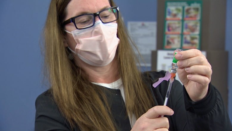 A health-care worker wearing a medical mask draws COVID-19 vaccine from a vial into a needle.