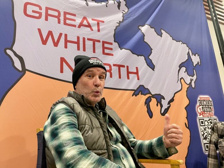 A person sits and gives a thumbs up before a backdrop showing a map of Canada reading 