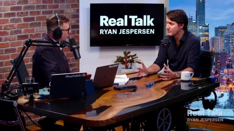 Two men talk in a podcast studio.