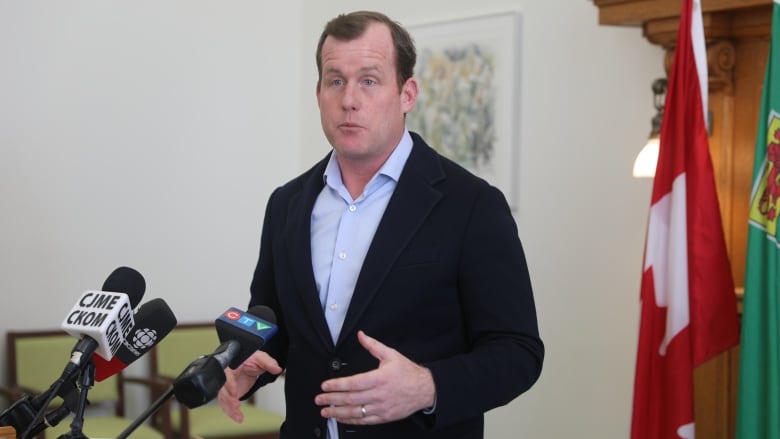 A man in a blue shirt and a black jacket stands at a podium. 