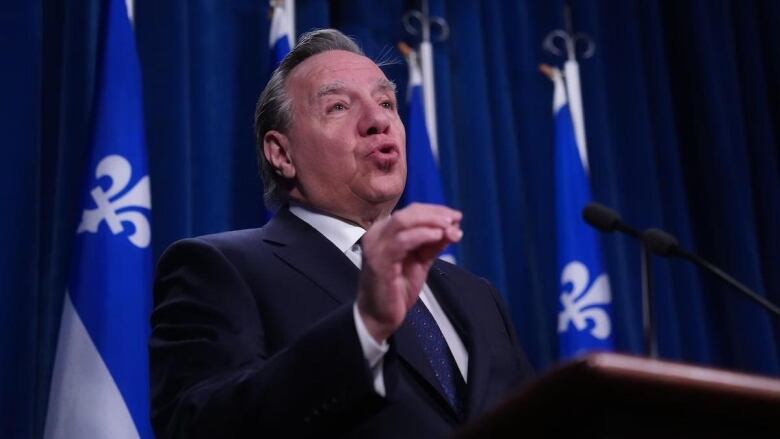 Man speaks at podium in front of Quebec flags