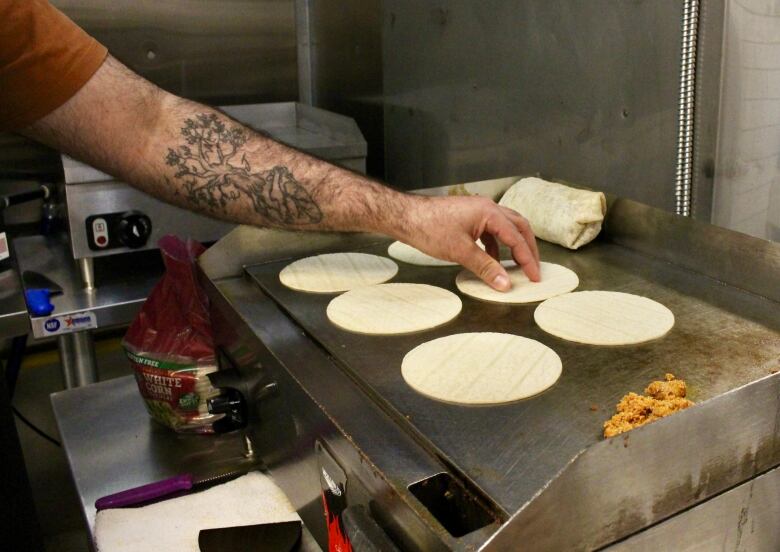 A man's hand is seen placing small round tortillas on a griddle.