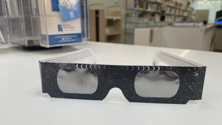 A pair of black paper glasses sit on a library counter. 