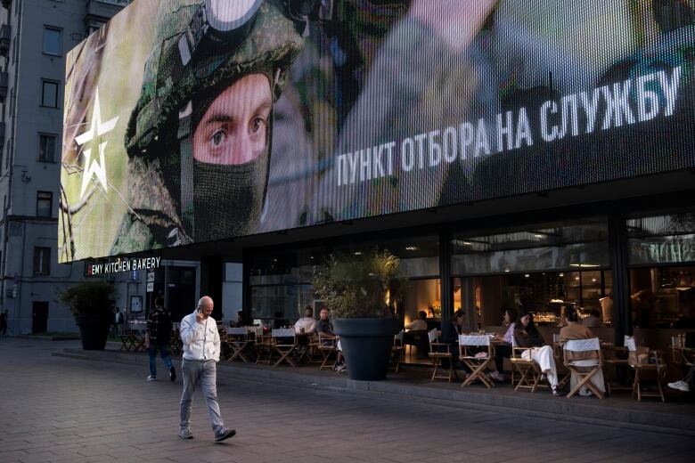 A man walks past a military recruitment poster in Russian.