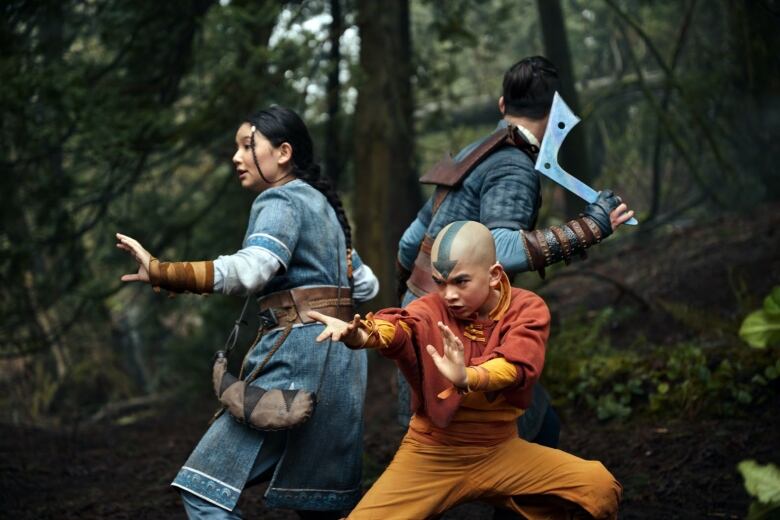 Three youths crouch in martial arts poses in a forest. 