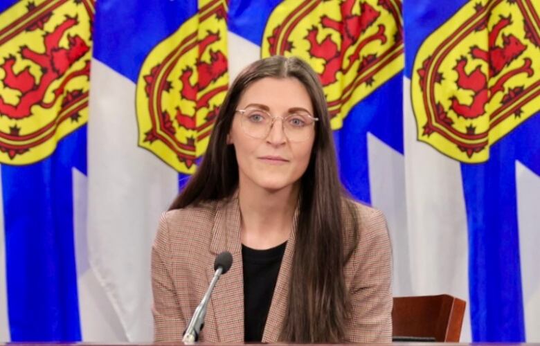 A woman sits in front of Nova Scotia flags.