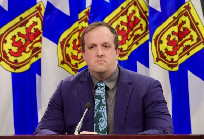 A man sits in front of Nova Scotia flags.