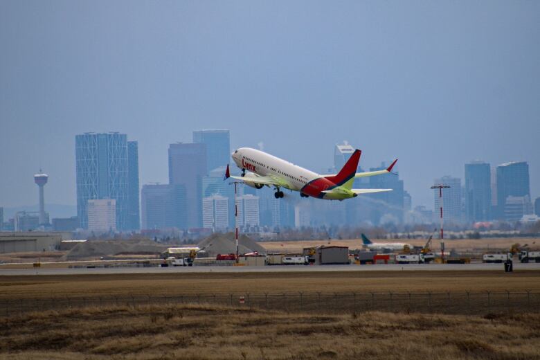 a plan takes off of a runway in the city of calgary. the city skyline is visible.