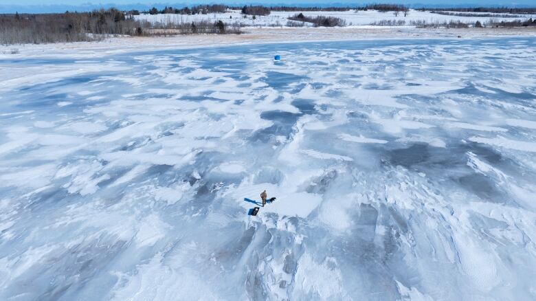 A man pulling a sled walks on the frozen ice as seen from the drone 