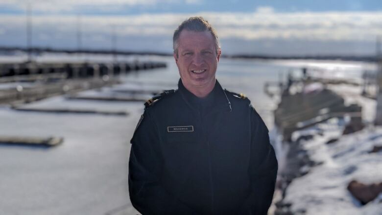 A man wearing a fisheries officer stands with a snowy harbour in the background