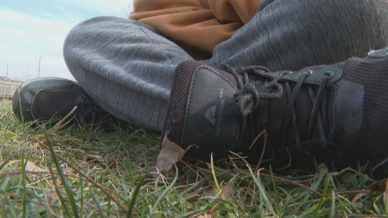 Close-up of feet of a teen sitting on grass.