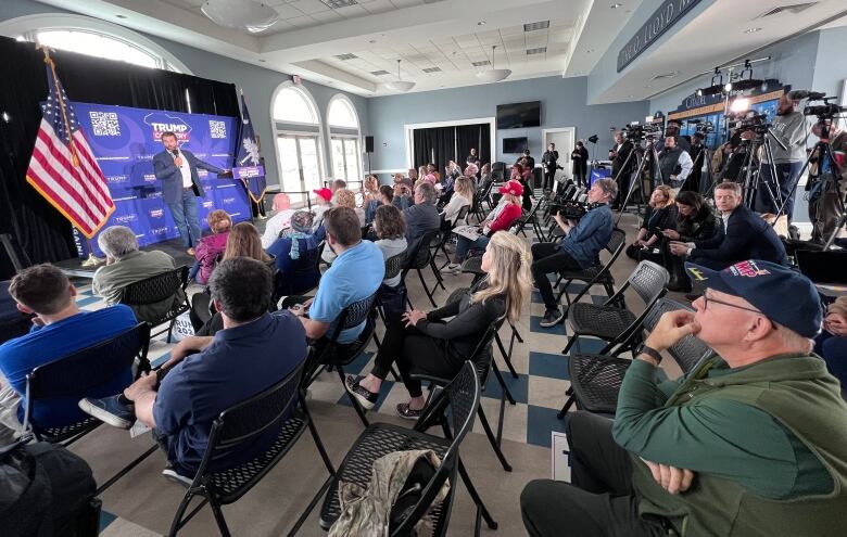 Crowd of several dozen people, and some TV cameras, assembled as Don Trump Jr speaks on stage