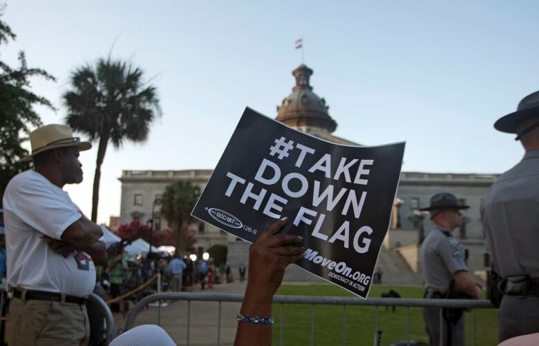 A hand holds a black sign with white lettering that reads 