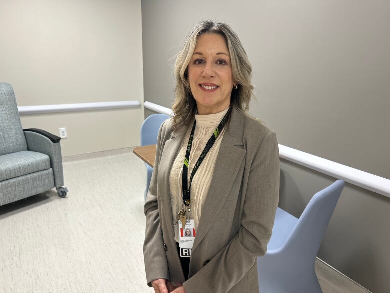 A woman with blonde hair waring a jacket stands in a health care facility. 