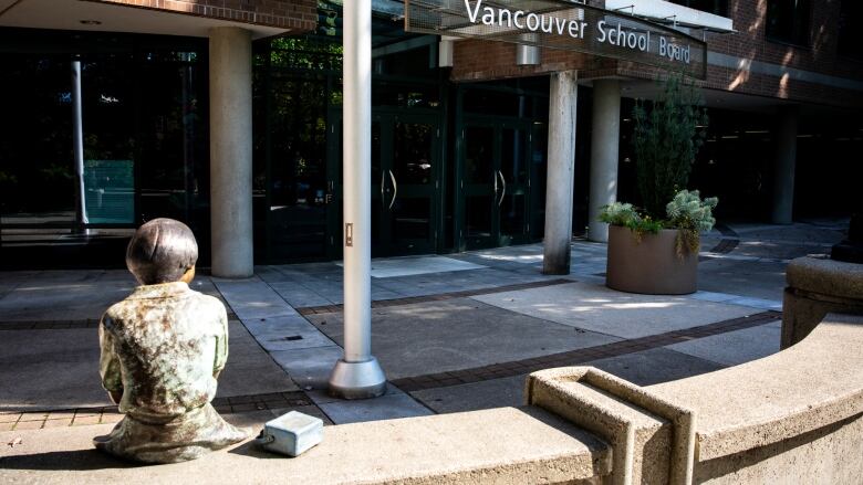 A statue of a schoolchild looks at a building that reads 'Vancouver School Board'.