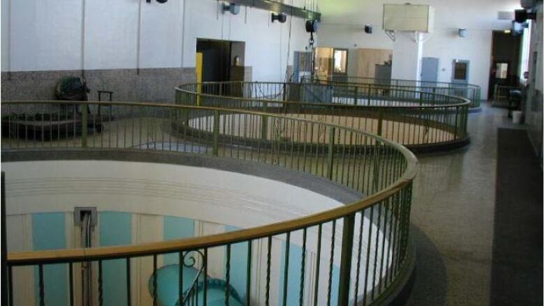 A photo shows the inside of a large industrial building. There are three large circular holes in the floor with railing around them.