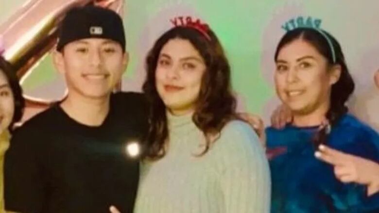 Three Hispanic people smile in a birthday party setting.