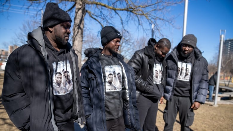 Four men stand side by side wearing shirts to honour shooting victim at a vigil.