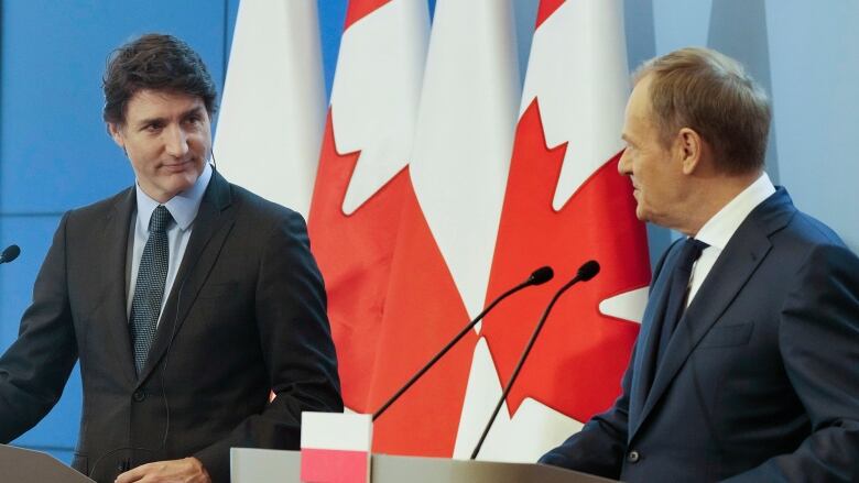 Two man stand at podiums looking at each other.