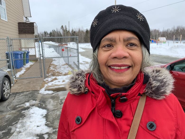 An African Nova Scotian woman wearing a black cap and red coat stands outdoors in the winter time. 