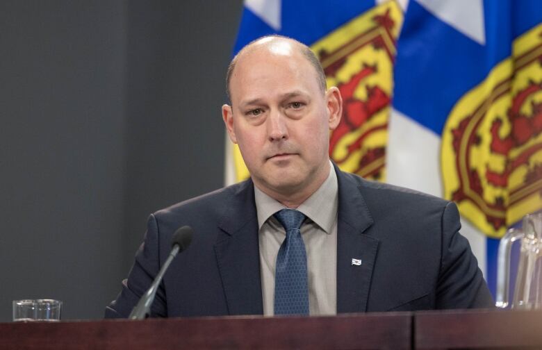 A bald man sits in front of flags.