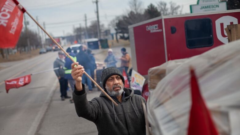 A man waving a Unifor flag on a picket line. 