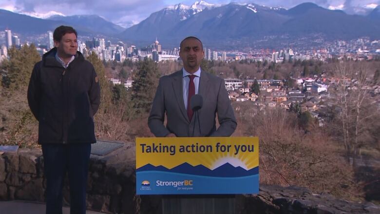 Two men stand together by a podium with the City of Vancouver in the background and snow-capped mountain.