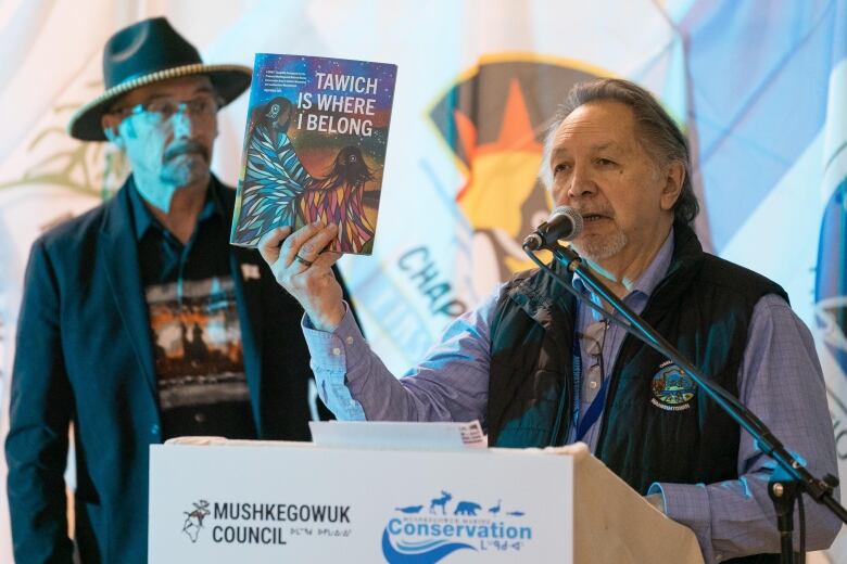 A man standing at a podium holding a pamphlet. 