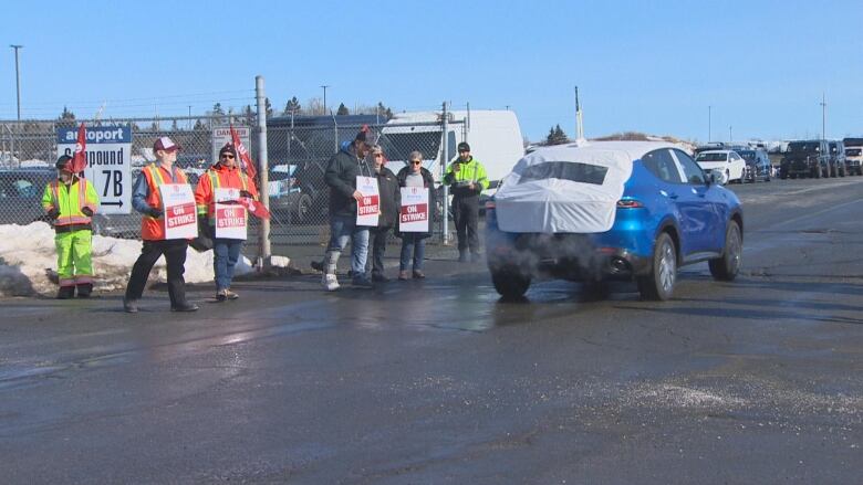 a blue vehicle drives past people with 'on strike' signs. 