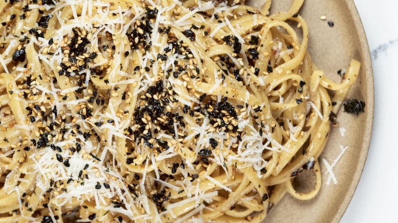 Closeup of pasta topped with shredded white cheese and furikake. It's on a beige plate. 