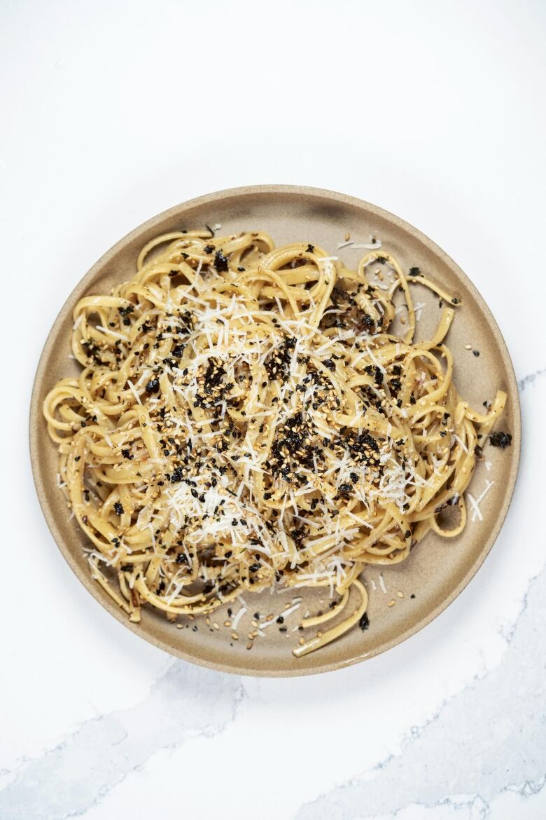 Overhead shot of pasta topped with shredded white cheese and furikake. It's on a beige plate.