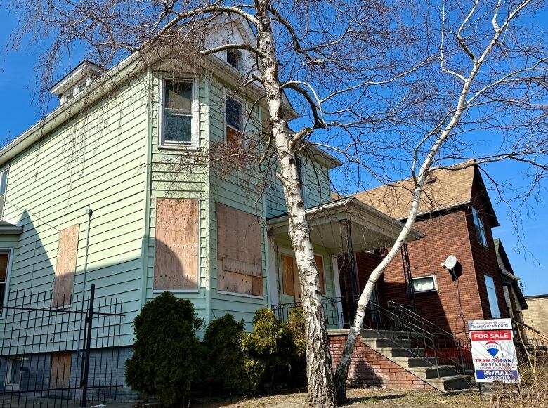 A large house in disrepair, with a real estate for sale sign.