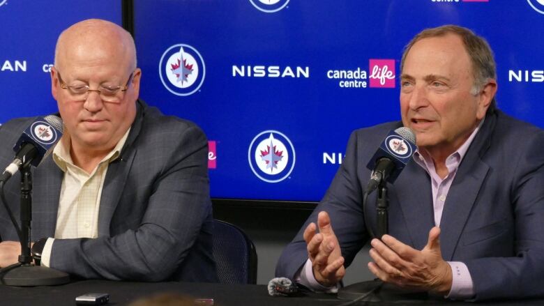 Two men are pictured answering questions in a press conference with a Winnipeg Jets logo in the background.