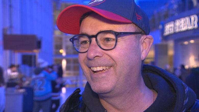 A man with glasses wearing a blue and red Winnipeg Jets hat is pictured in a closeup shot. 