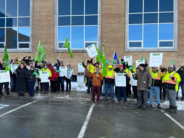 People in winter coats standing outside brick building, waving green flags and holding signs.