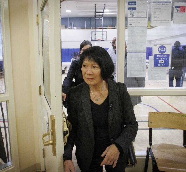 A woman in a dark coat walks through a door.